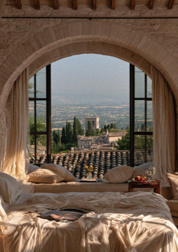A rustic-elegant Assisi hotel room with an arched window framing the valley