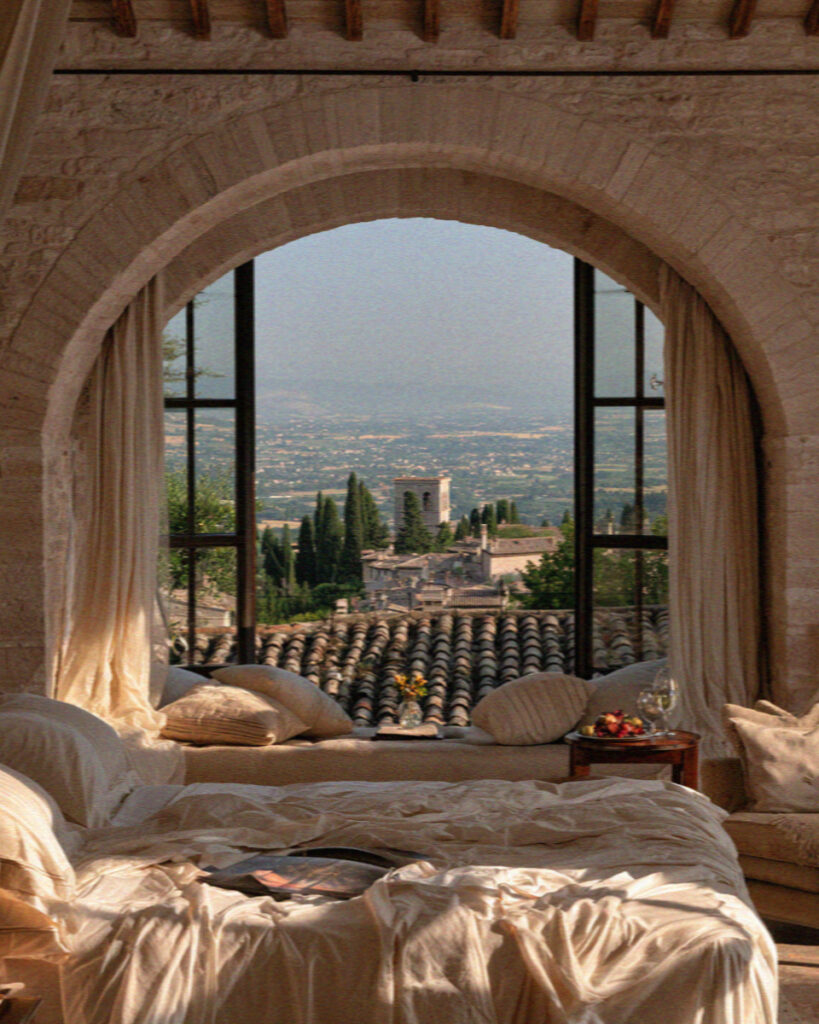 A rustic-elegant Assisi hotel room with an arched window framing the valley