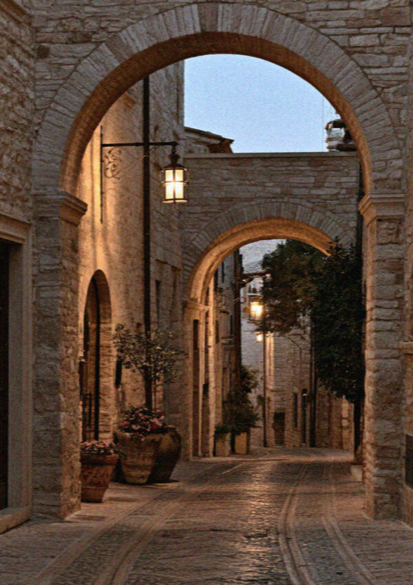 A medieval Assisi alley at twilight with wrought-iron lamps glowing on pale stone