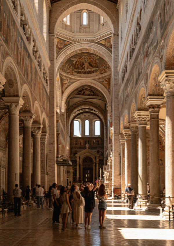 Visitors standing in the sunlit frescoed nave of the basilica in Assisi