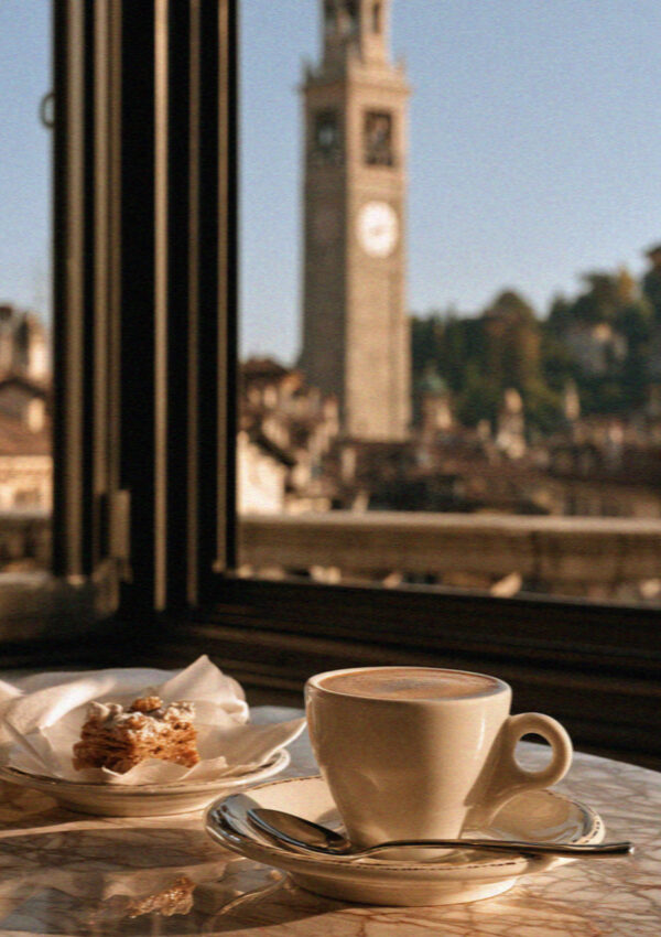 A coffee and pastry by a window with the Bergamo tower beyond
