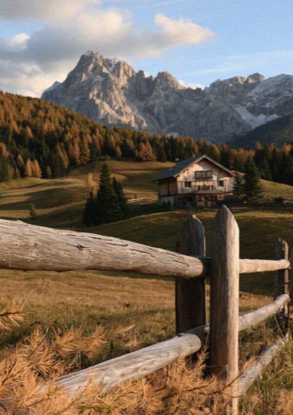 An autumn meadow with a chalet and larches below Dolomite peaks