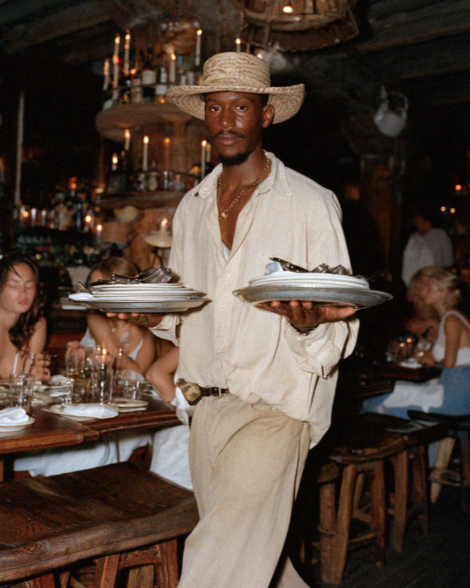 A veteran waiter carrying plates in a candlelit Cortina dining room