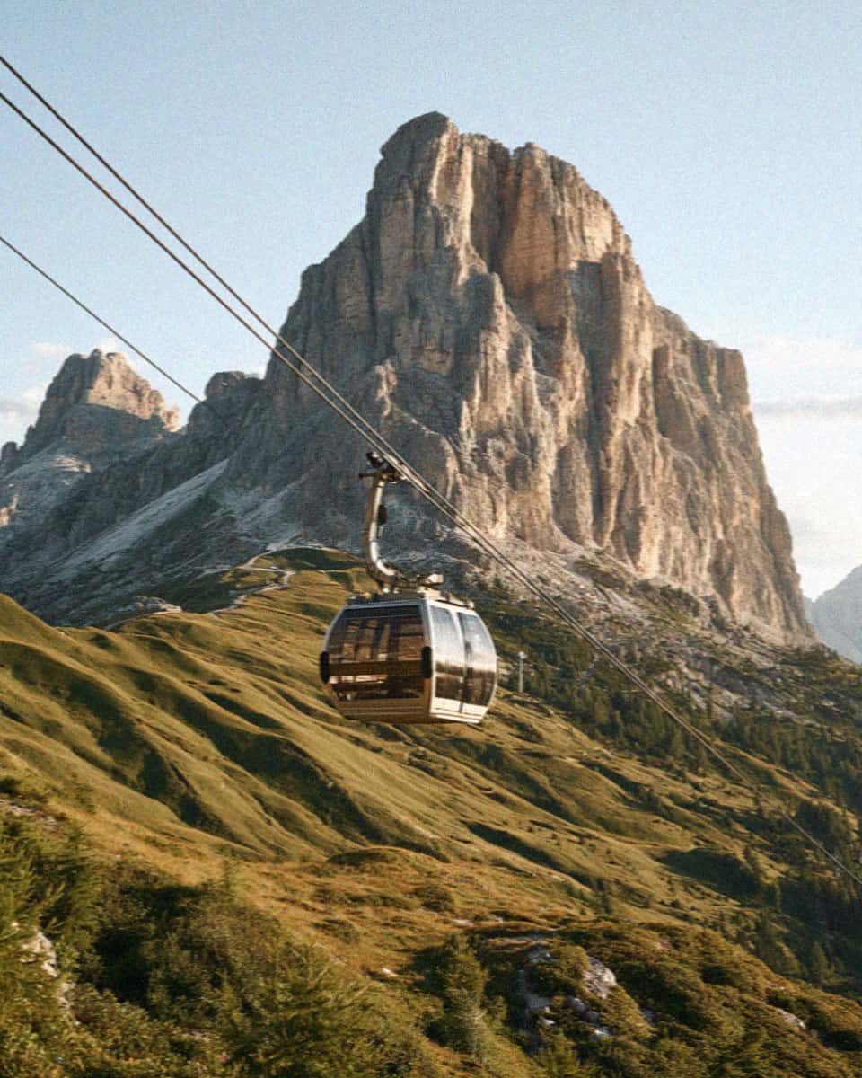 A gondola cable car climbing below a great Dolomite peak