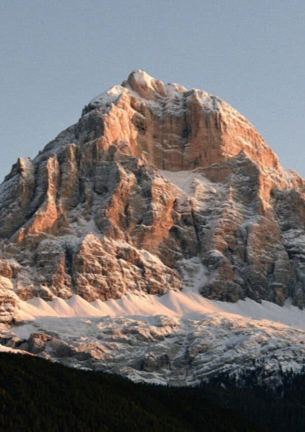A pyramidal Dolomite peak dusted with snow in warm evening light