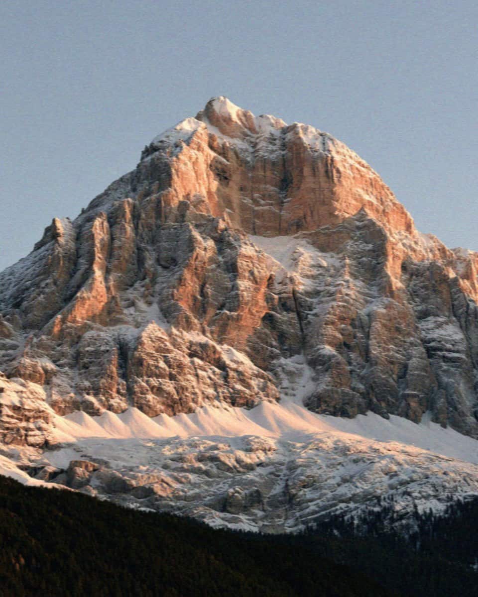 A pyramidal Dolomite peak dusted with snow in warm evening light