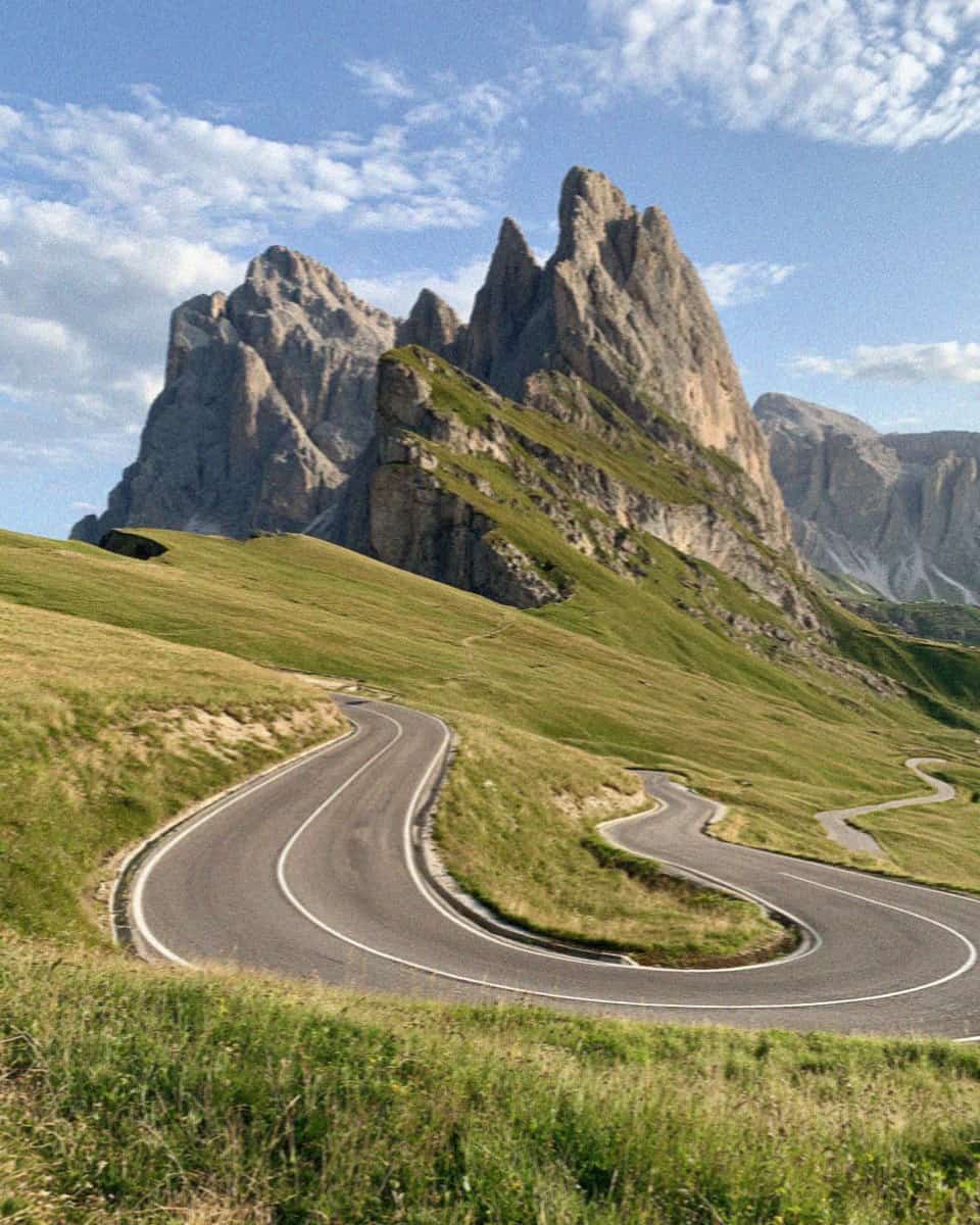 A hairpin mountain pass road climbing through meadows in the Dolomites