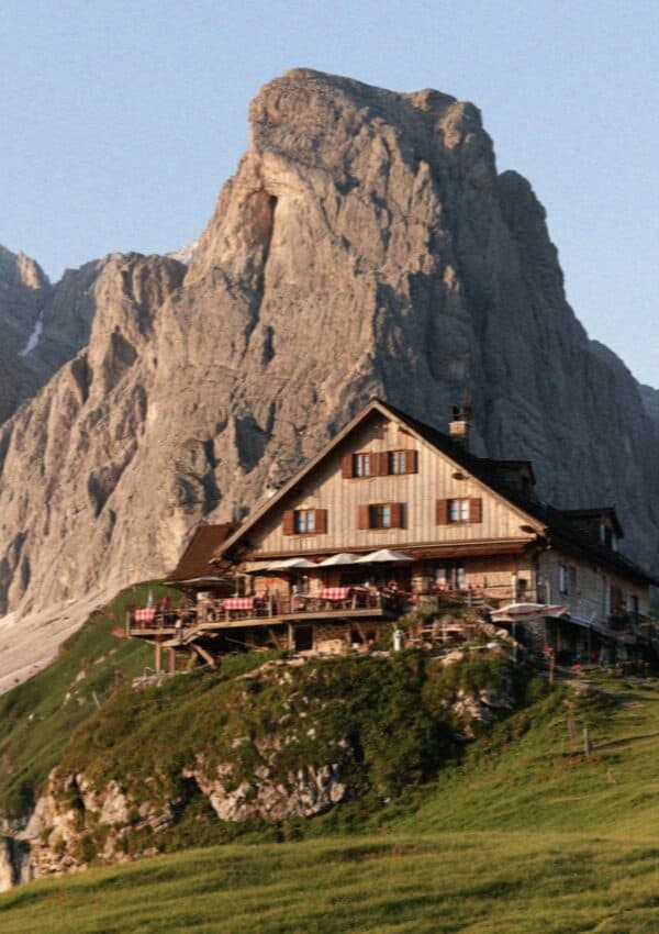 A traditional wooden rifugio mountain hut on a green shoulder in the Dolomites