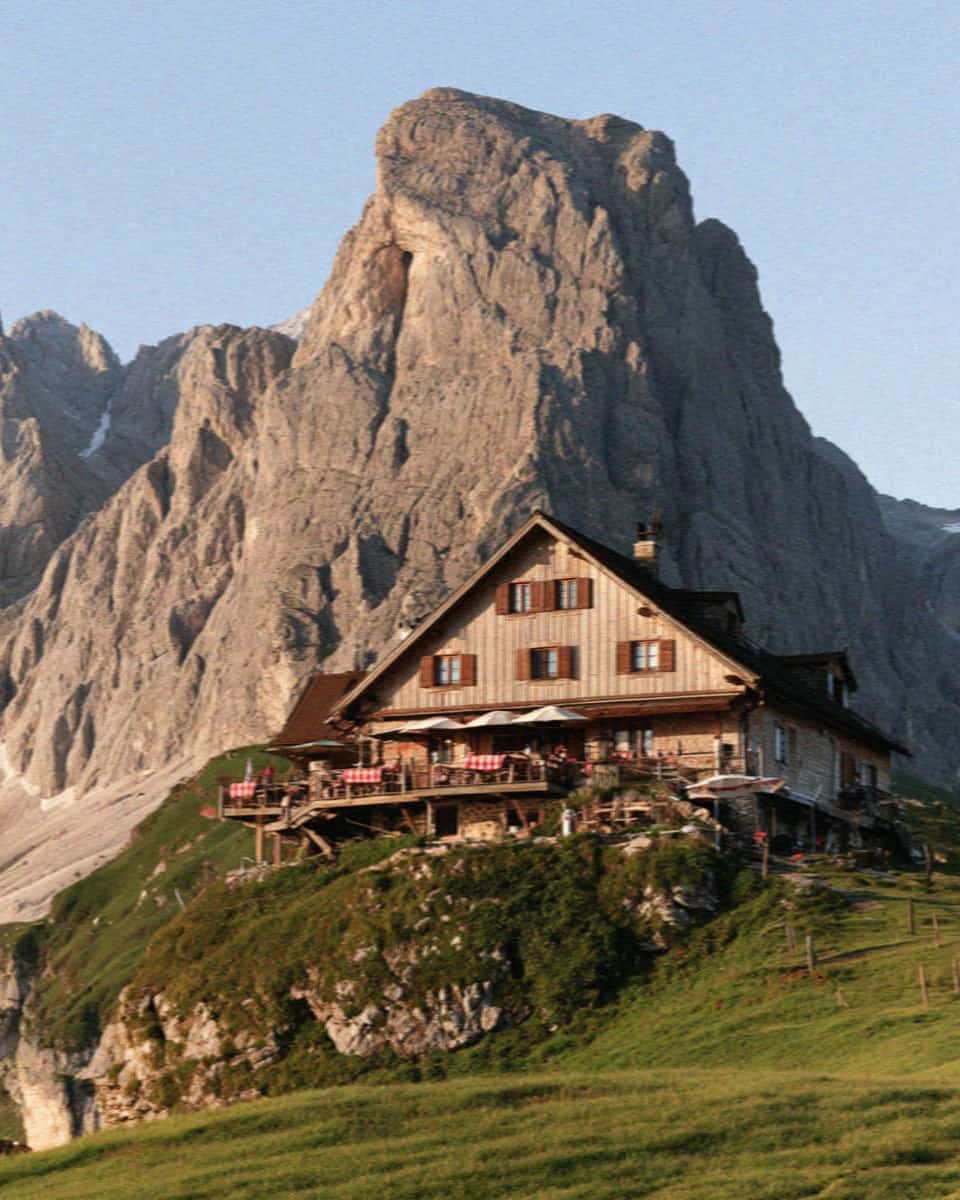 A traditional wooden rifugio mountain hut on a green shoulder in the Dolomites