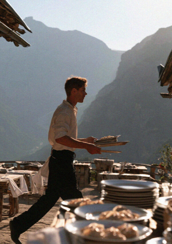 A rifugio waiter carrying plates across a terrace in the Dolomites