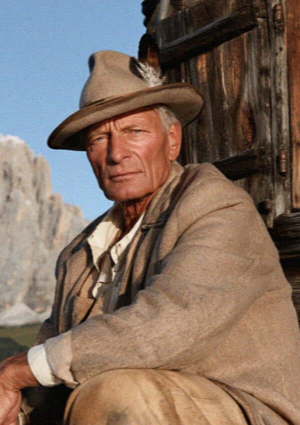 An older South Tyrolean man in a feathered felt hat by a wooden chalet
