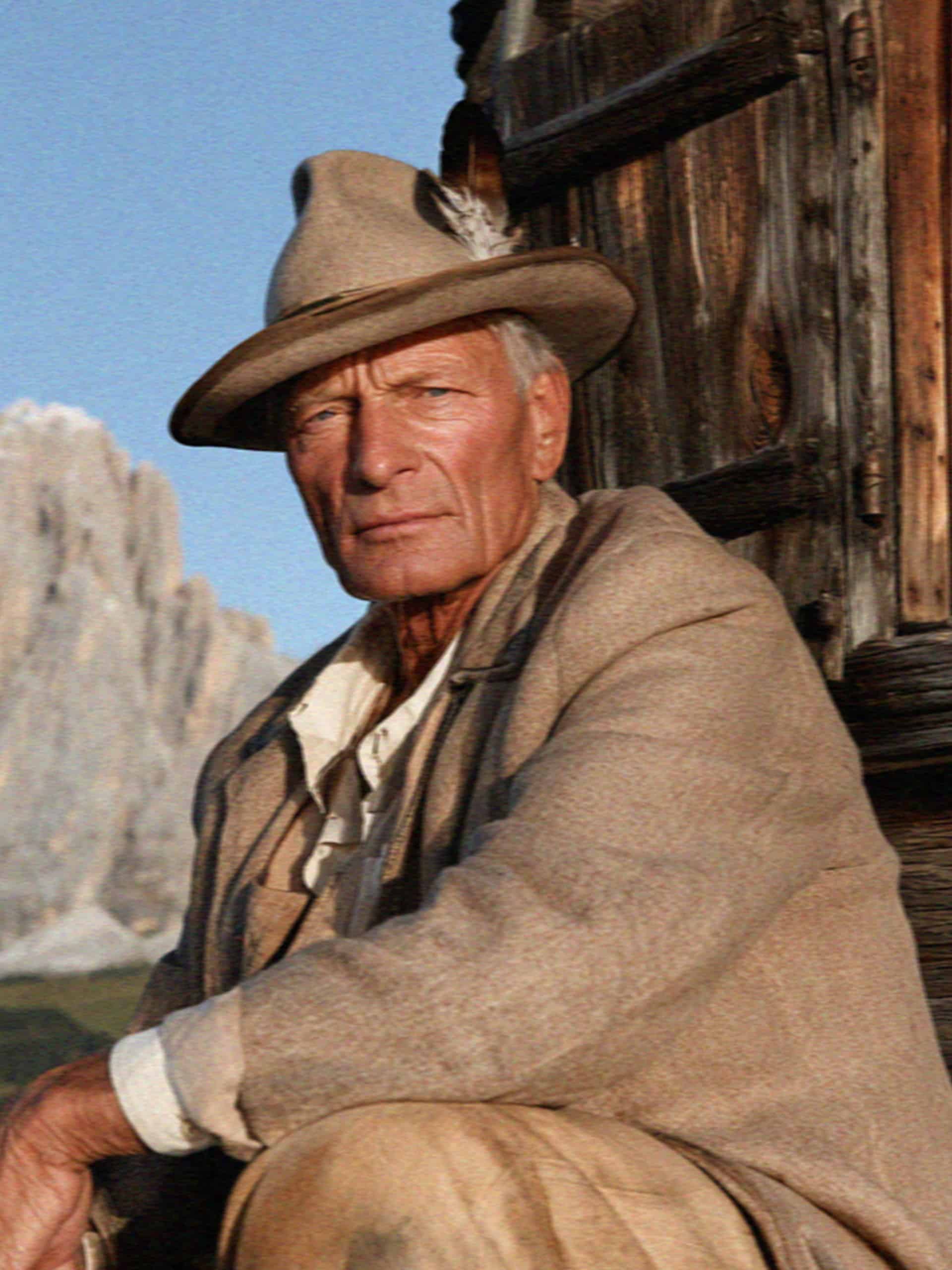 An older South Tyrolean man in a feathered felt hat by a wooden chalet