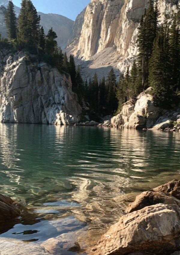 A turquoise glacial lake below pale rock cliffs and pines in the Dolomites
