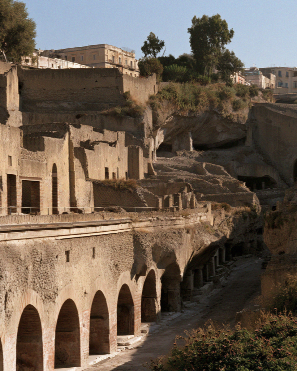 The excavated town of Herculaneum sunk far below the modern street level, arched chambers along the old shoreline, no people
