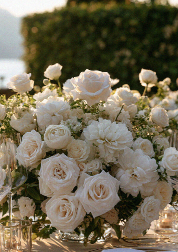 A lush white and green wedding floral arrangement on a lakeside table on Lake Como
