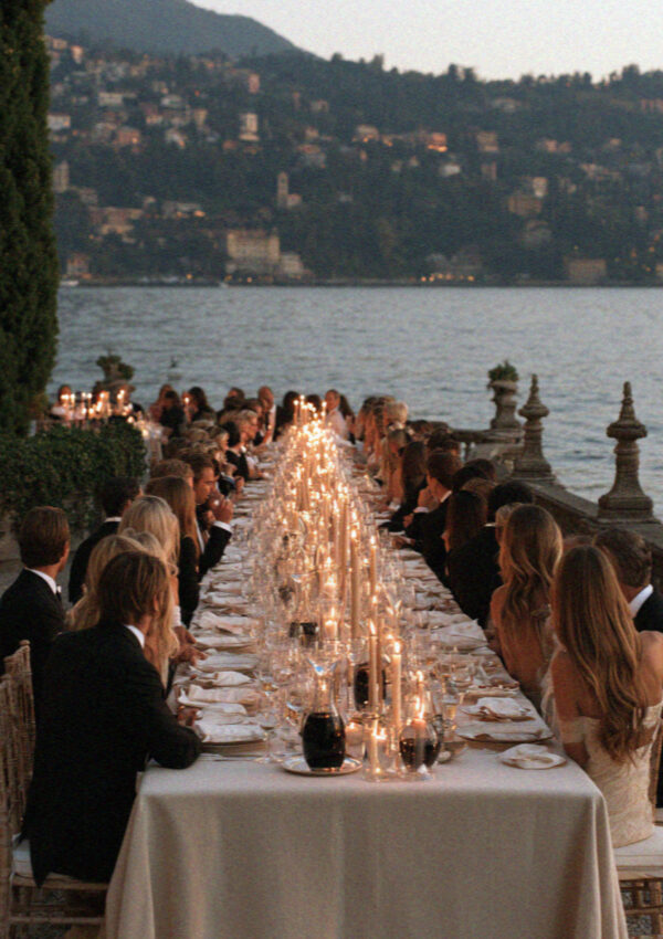 A long communal welcome dinner table set beside the water on Lake Como