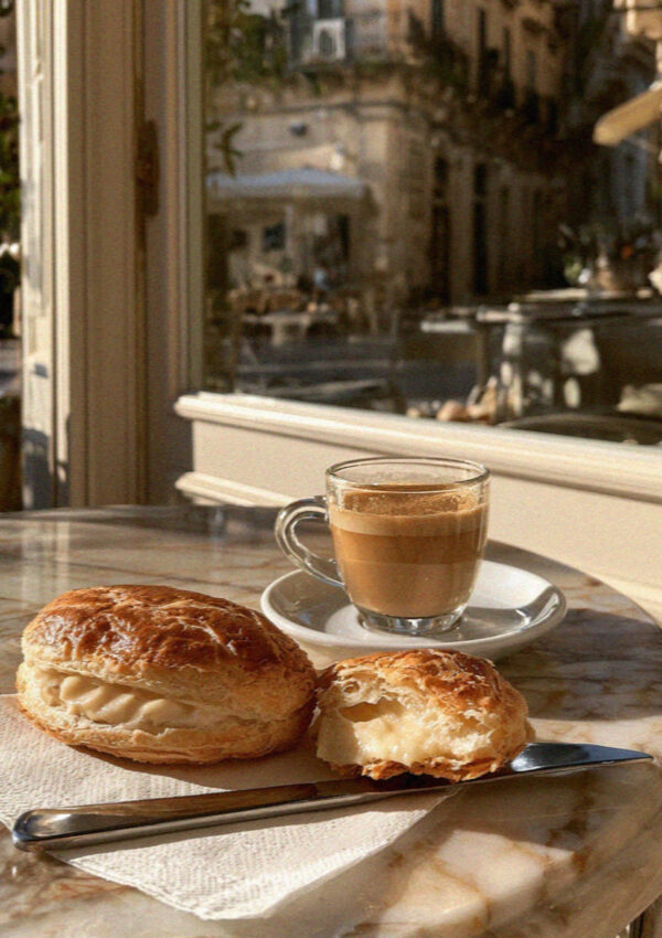 A pasticciotto broken open beside an espresso on a marble cafe table in Lecce
