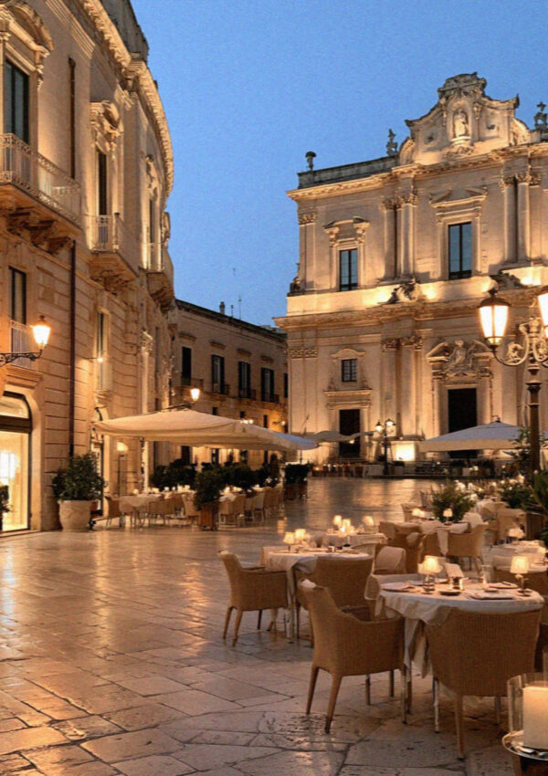 A baroque square in Lecce at dusk, warm lit facades against a deep blue sky
