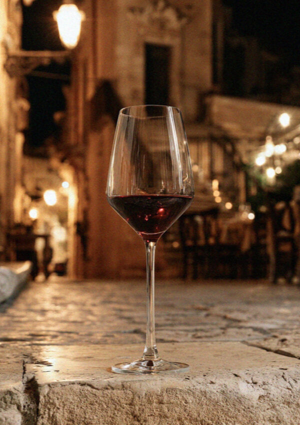 A glass of red wine on a worn limestone step in Lecce at night