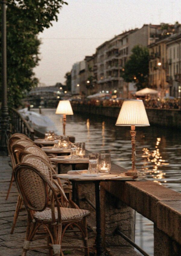Bar tables and lamps along a Milan canal at dusk