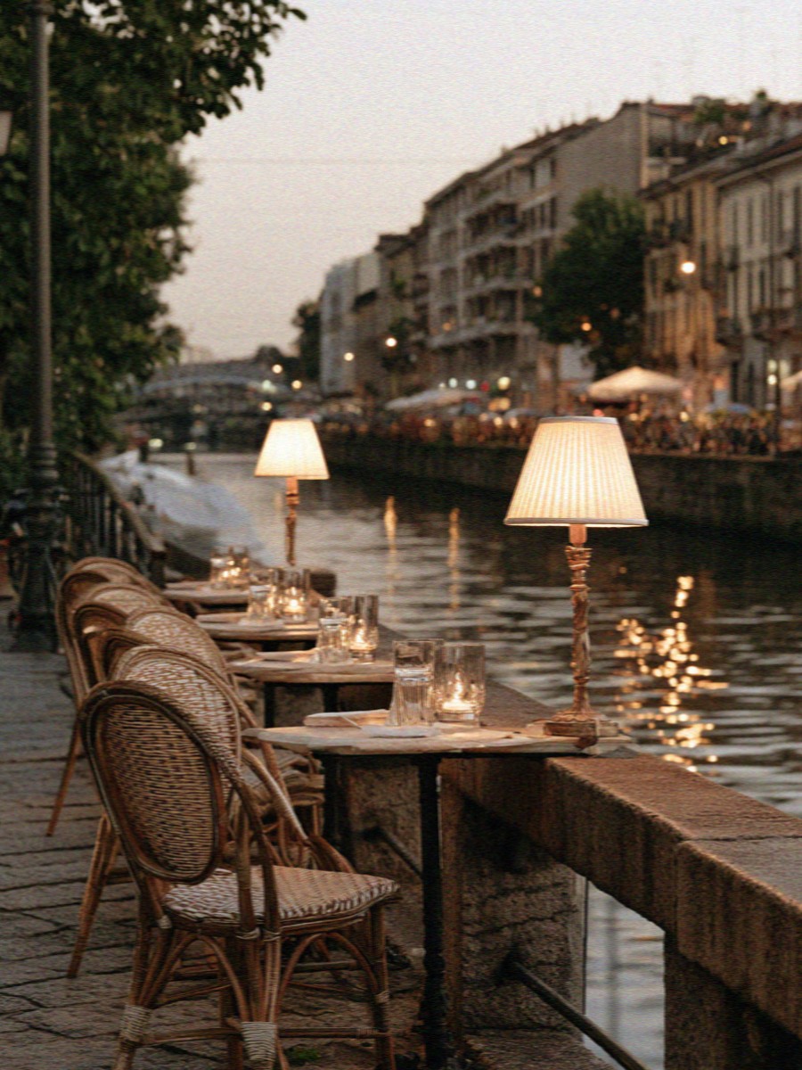 Bar tables and lamps along a Milan canal at dusk
