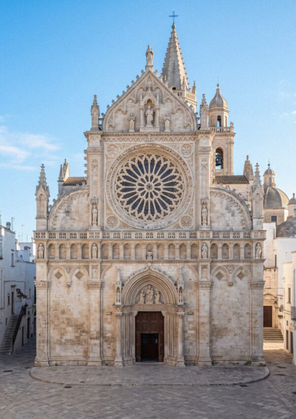 The pale limestone facade and large carved rose window of Ostuni Cathedral in Puglia