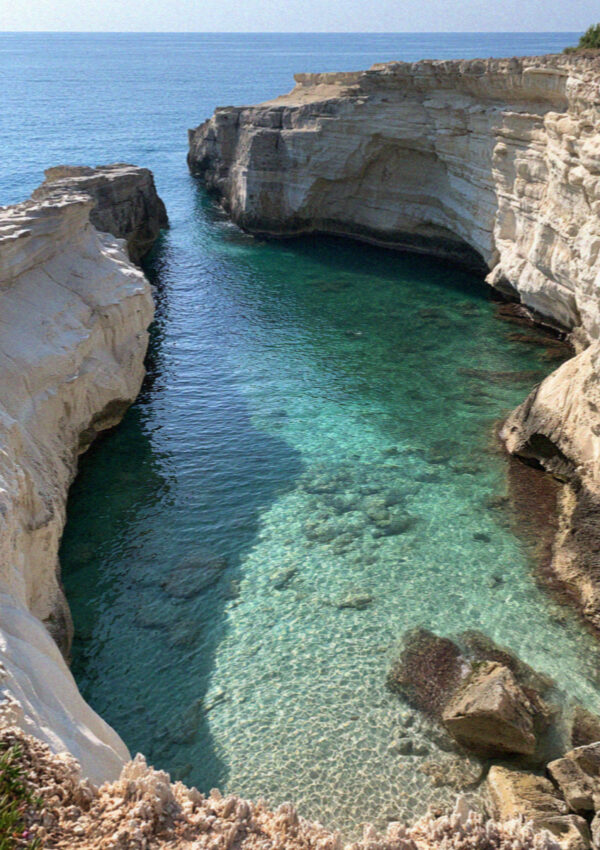 A narrow cove of clear turquoise water cut into white limestone on the Ostuni coast