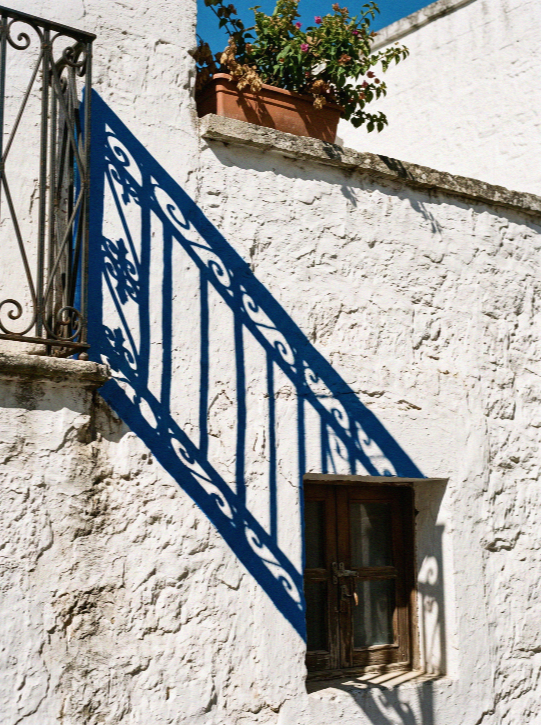 A thickly lime-washed white wall in Ostuni with a hard blue shadow falling across it