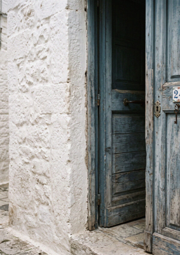 Thickly lime-washed white wall meeting a faded blue wooden door in Ostuni in Puglia