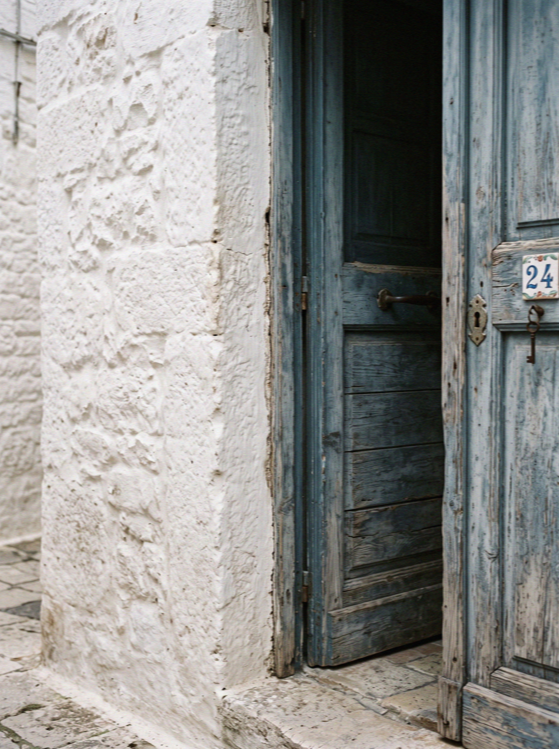 Thickly lime-washed white wall meeting a faded blue wooden door in Ostuni in Puglia