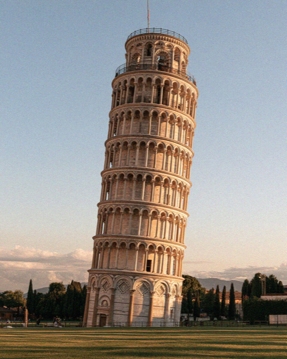The Leaning Tower of Pisa tilting on the grass of Piazza dei Miracoli at golden hour