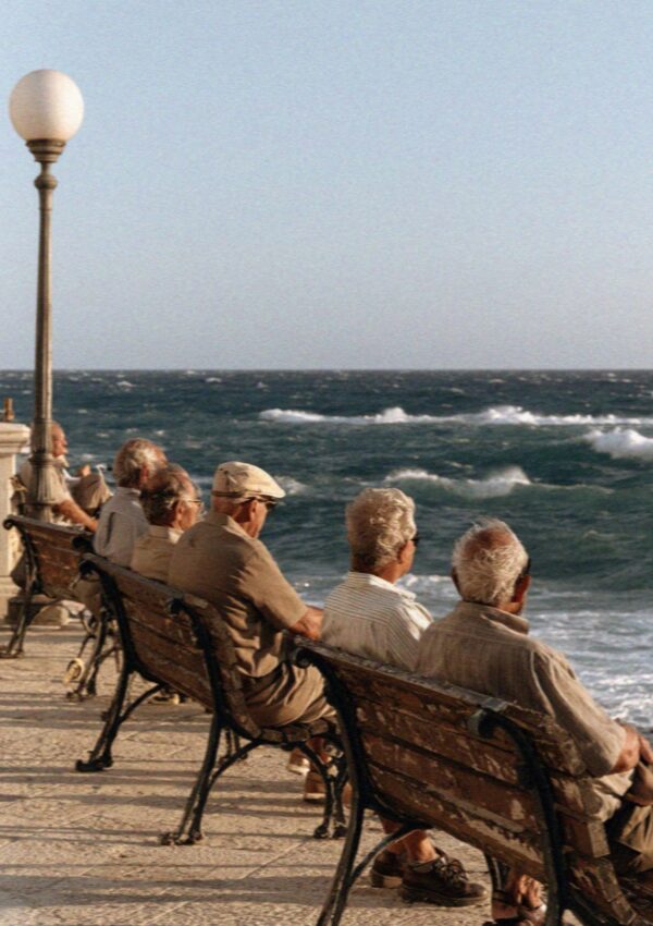Older men on a seafront bench facing a rough sea at Polignano a Mare