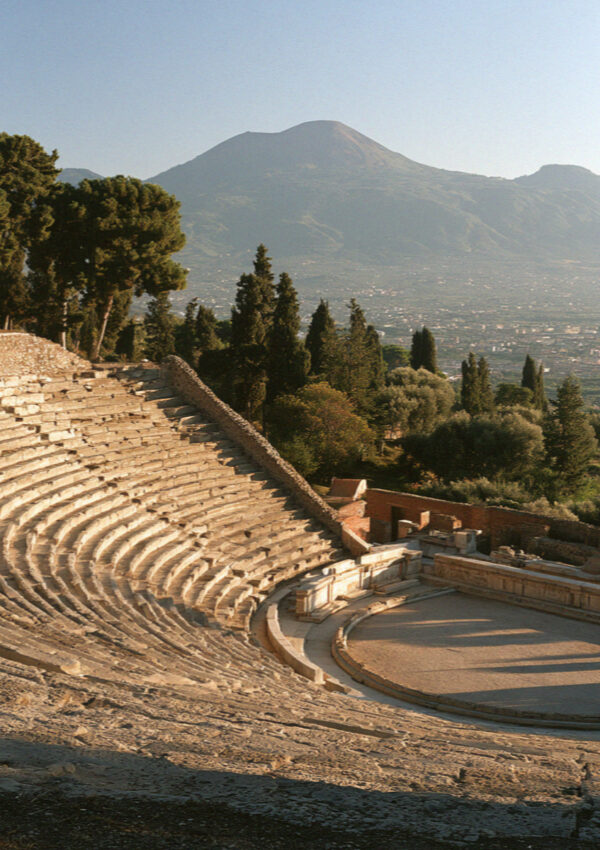 The stone tiers and oval arena of the ancient amphitheatre in Pompeii seen from high on the seating in warm late light, no people