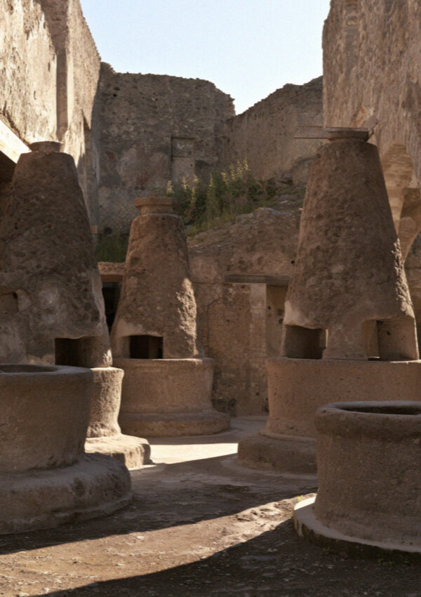 The tall conical volcanic stone grinding mills of an ancient bakery in Pompeii under hard high sun, no people