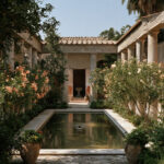 A restored garden courtyard in Pompeii ringed by small columns with oleander in flower and a shallow rectangular pool, no people