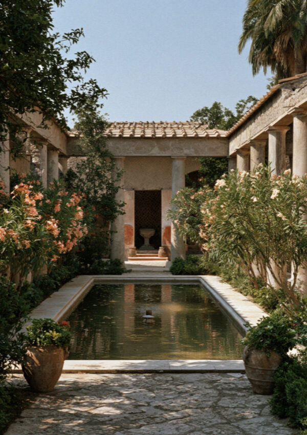A restored garden courtyard in Pompeii ringed by small columns with oleander in flower and a shallow rectangular pool, no people