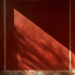Close-up of a deep red painted plaster wall in Pompeii with a fine ochre border and flaking edges