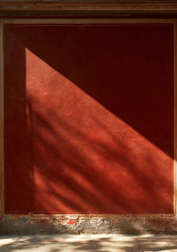 Close-up of a deep red painted plaster wall in Pompeii with a fine ochre border and flaking edges