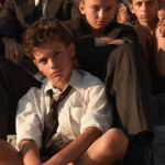 A group of Italian schoolchildren sitting with their teacher on ancient stone steps in Pompeii in late morning light