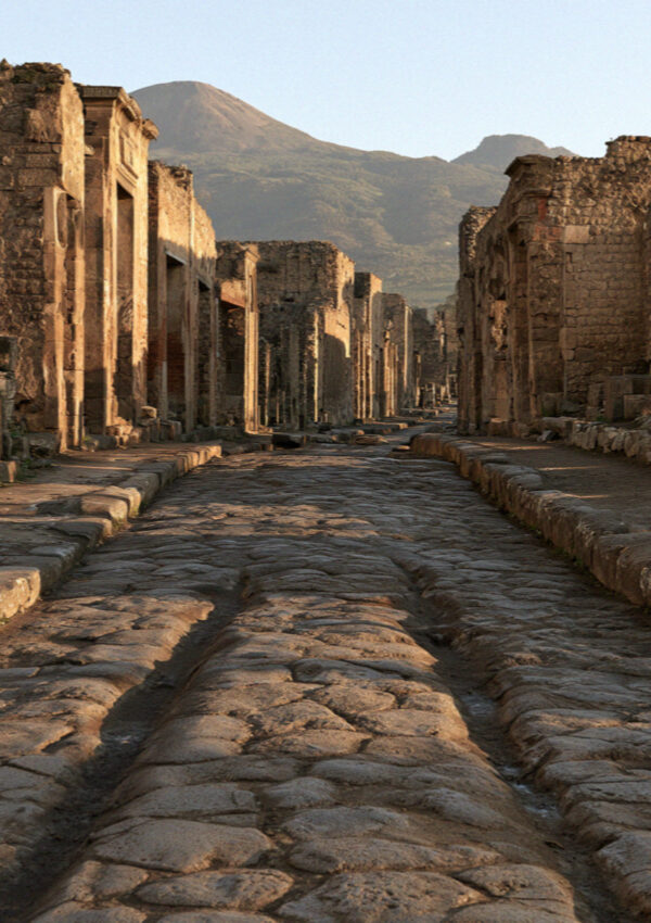 An ancient paved street in Pompeii with raised stone crossing blocks and deep cart ruts worn into the basalt, no people