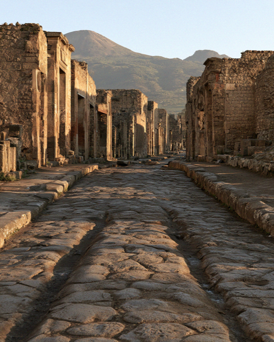 An ancient paved street in Pompeii with raised stone crossing blocks and deep cart ruts worn into the basalt, no people