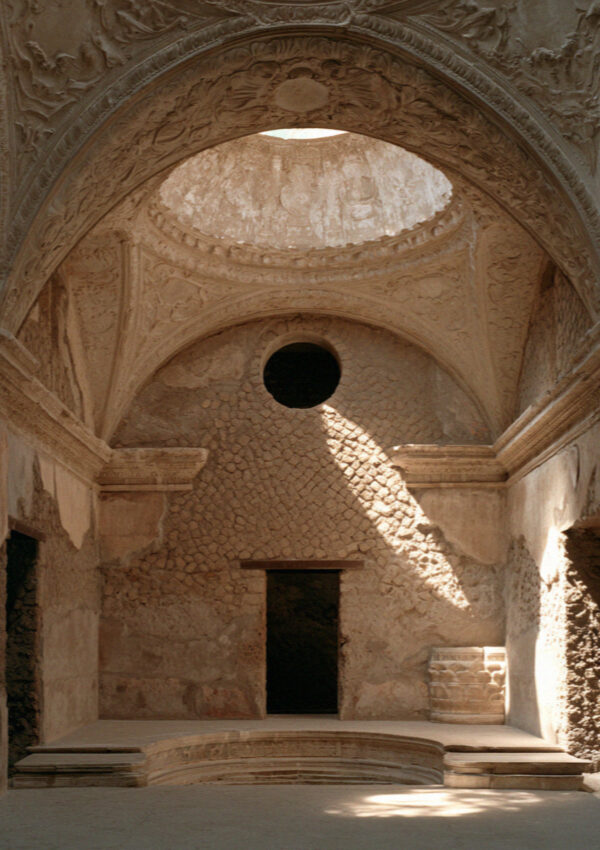A vaulted ancient bath chamber in Pompeii with a moulded stucco ceiling and a shaft of light from a round opening above, no people