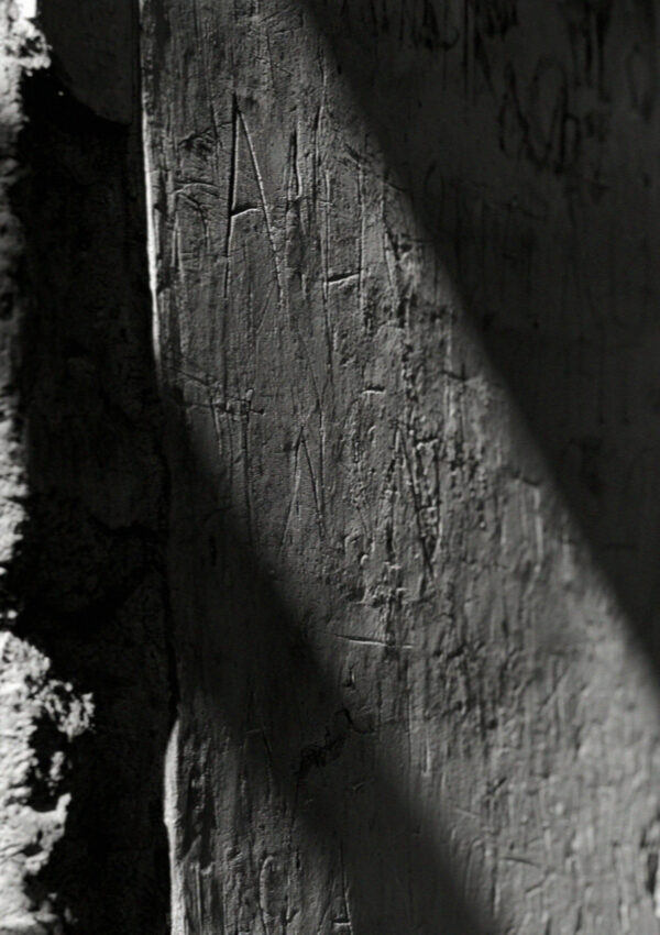 Close-up of scratched ancient lettering in a stucco wall in Pompeii with raking light across the surface