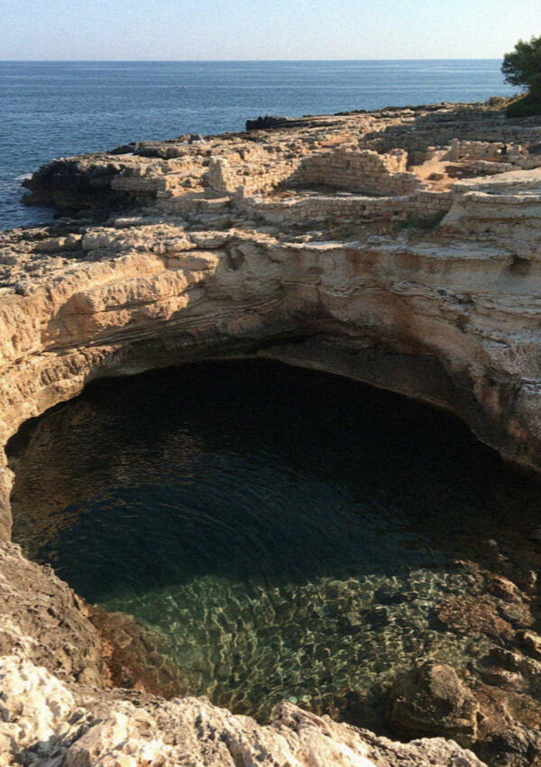 A circular limestone sinkhole open to the sea on the Adriatic coast of the Salento, near Lecce