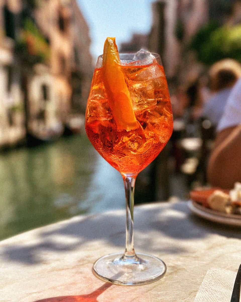 An Aperol spritz on a marble table by a Venetian canal