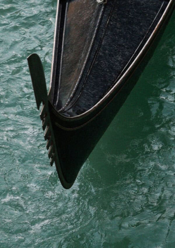 The steel ferro prow of a Venetian gondola on green canal water