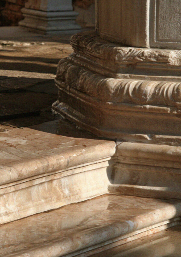 Close-up of worn marble column bases and steps polished smooth in the warm Venetian light