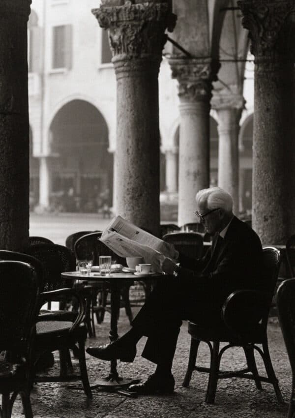 An older man reading the newspaper at a cafe under the arcades of Piazza delle Erbe, Verona