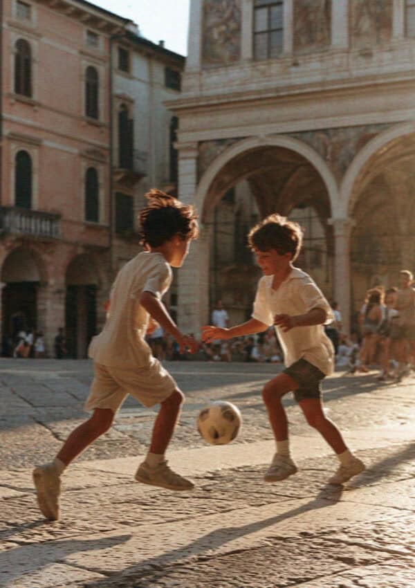 Two boys playing football in a Verona piazza at golden hour