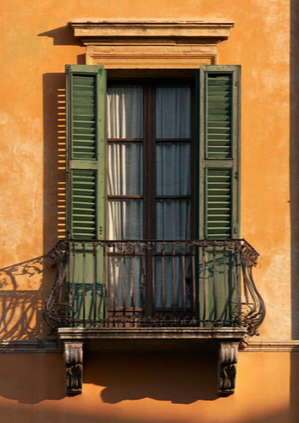 A shuttered window and wrought-iron balcony on an ochre Verona palazzo